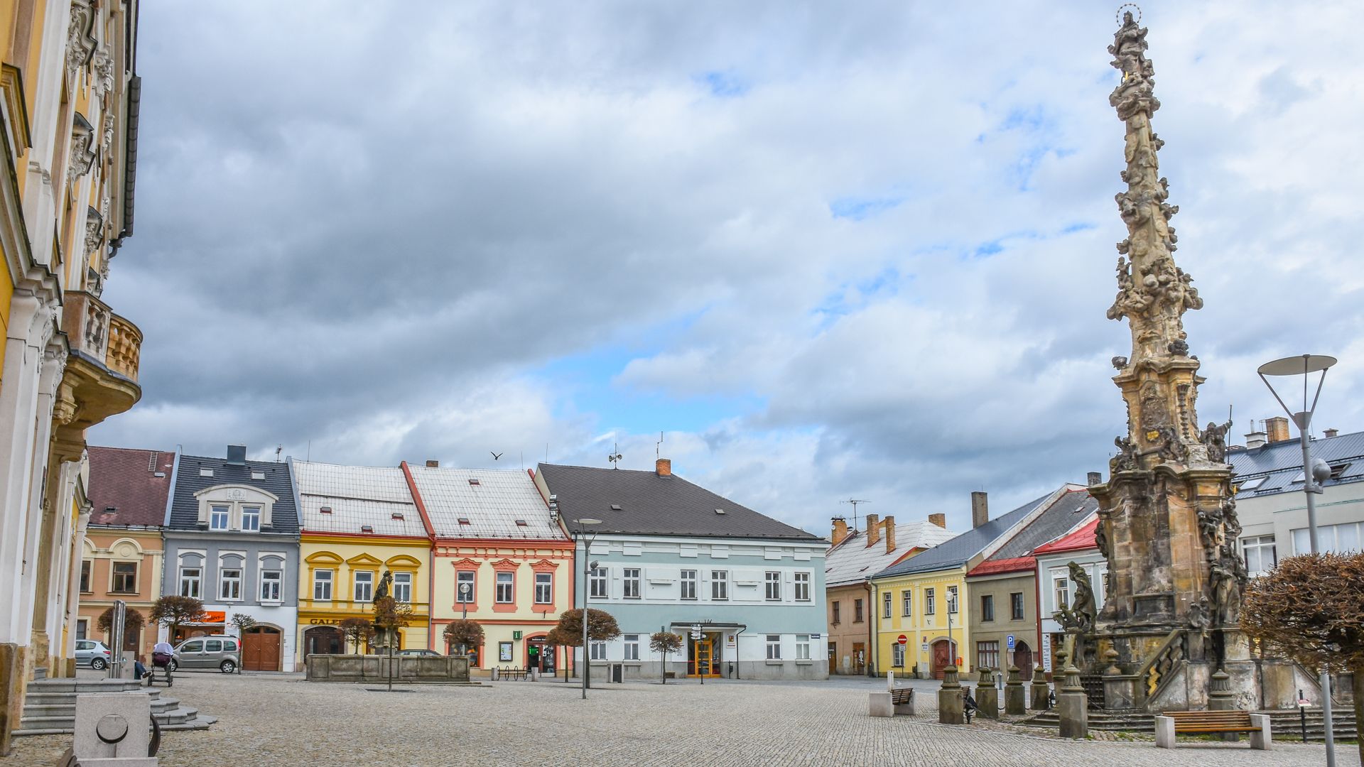 Cobblestone town square with a tall ornate stone column and colorful historic buildings