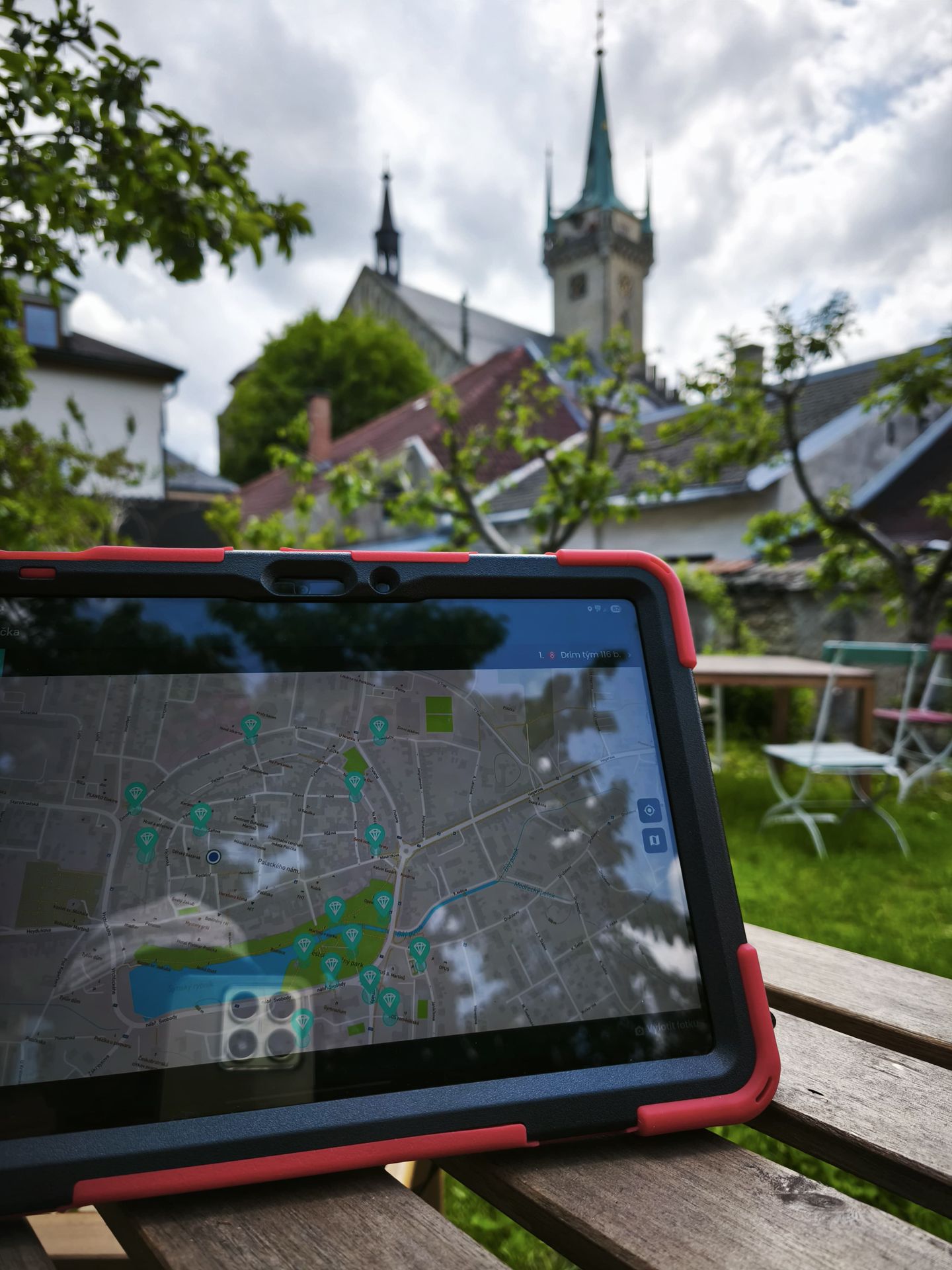 Tablet displaying a GPS game map on an outdoor table with a church tower in the background