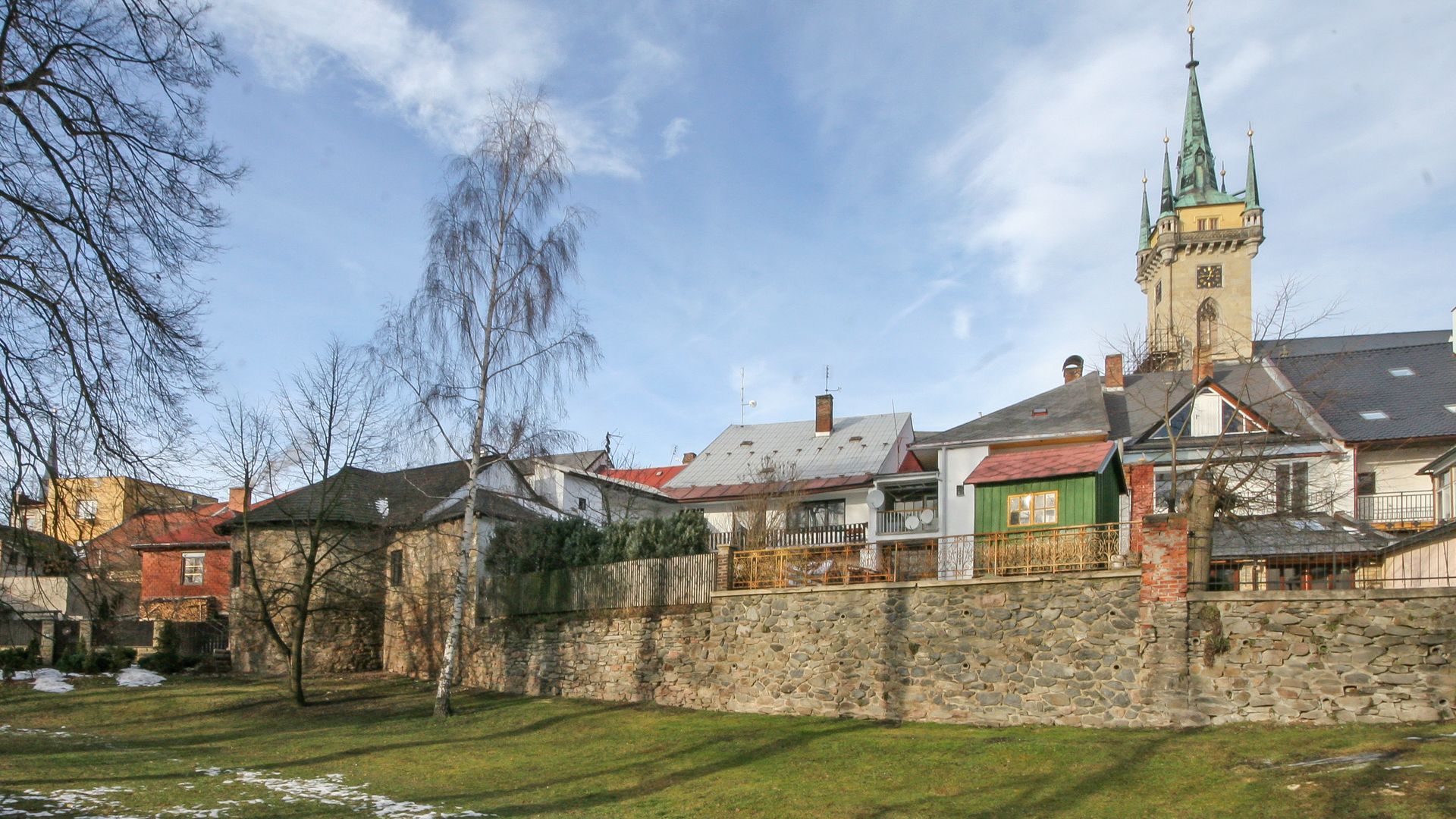 Stone fortification wall and residential buildings beneath a tall tower with a clock and spire