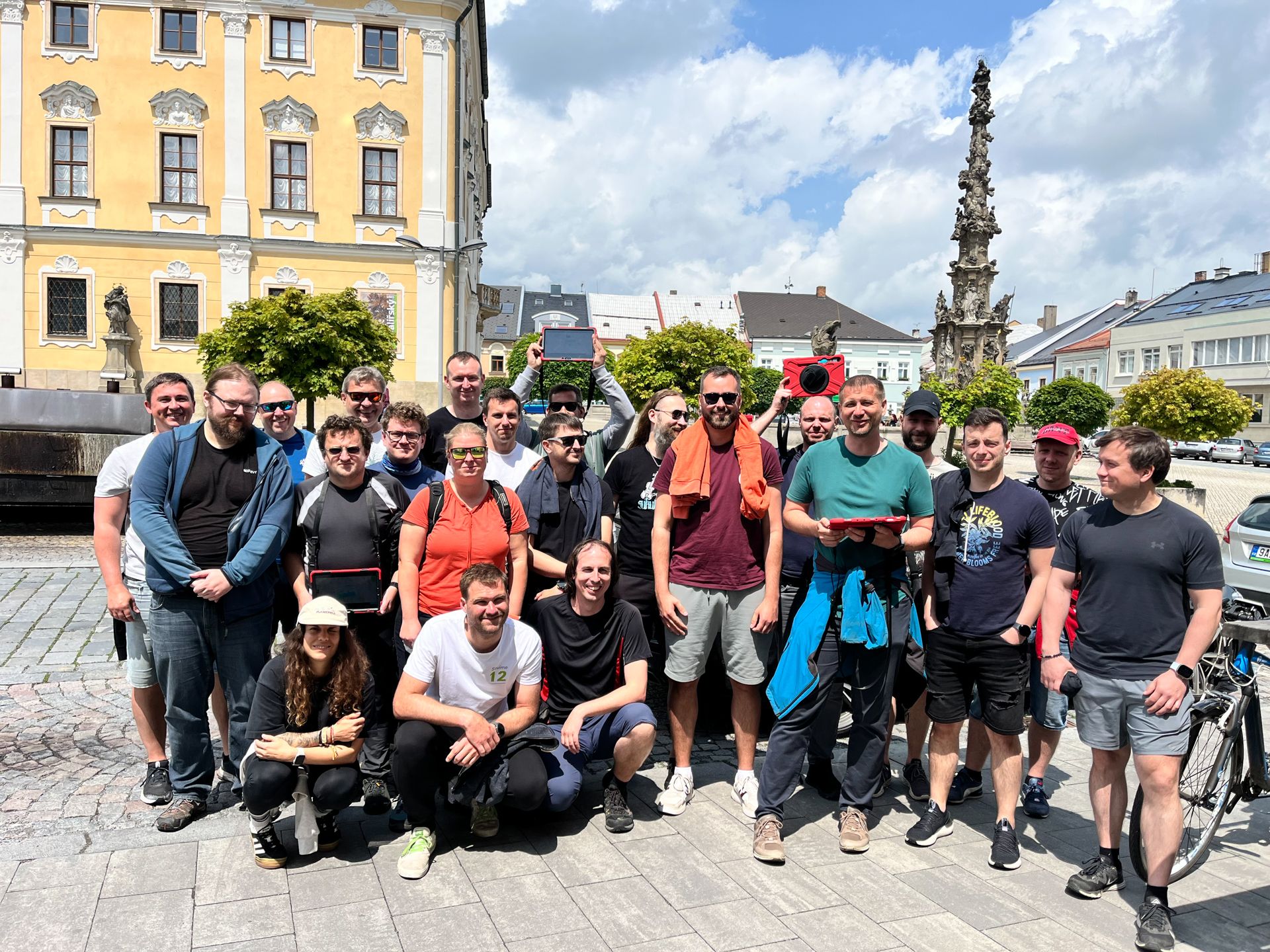 Group of people posing outdoors on a historic town square holding tablet computers
