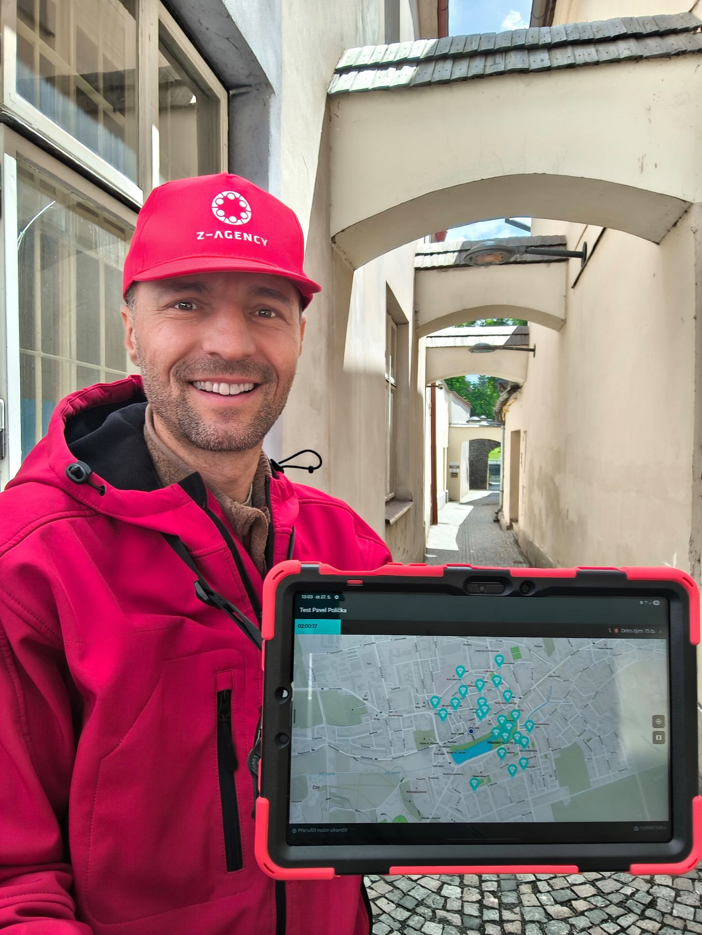 Man holding a tablet displaying a map with pin markers in a narrow cobblestone alley