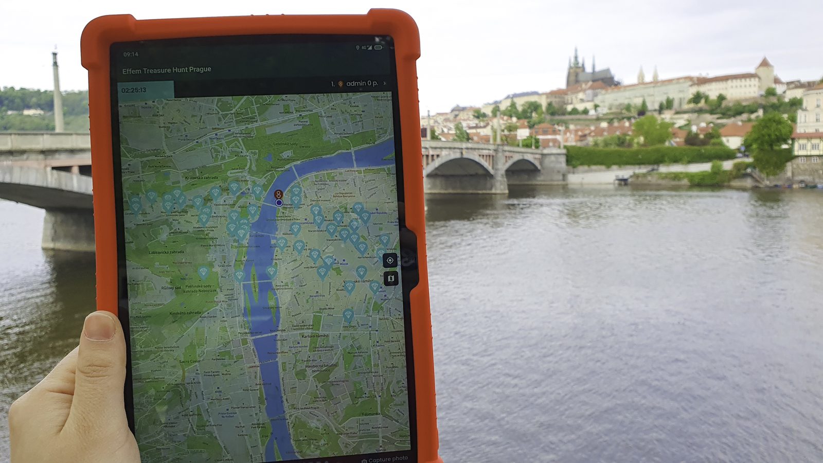 Tablet a Treasure Hunt Prague játéktérképével, a háttérben a prágai vár és a Moldva